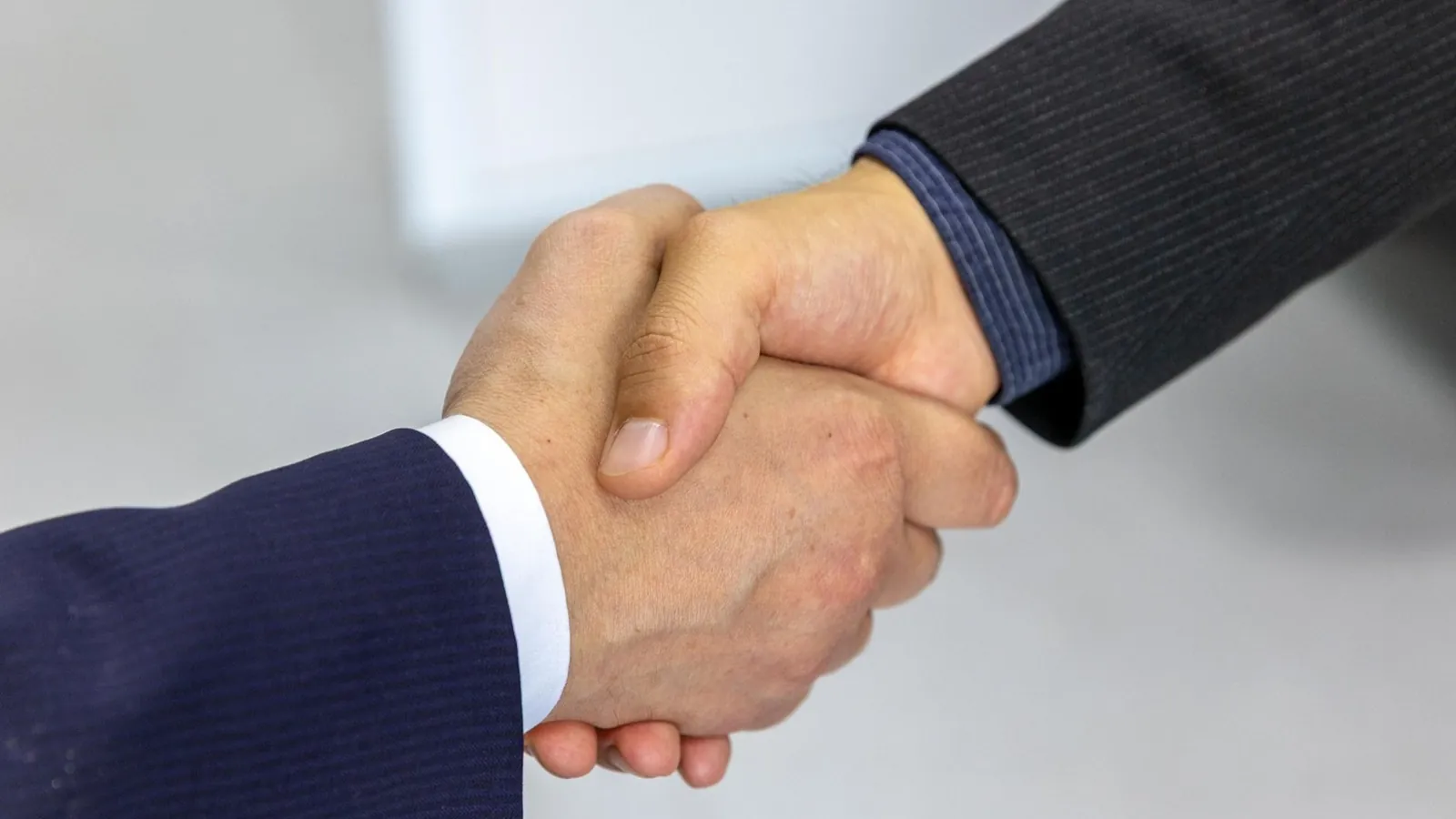 Zwei Personen im Anzug geben sich die Hand als Symbol fuer eine einvernehmliche Einigung