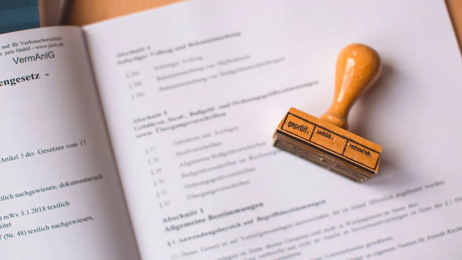 Aufgeschlagenes Gesetzbuch mit Pruefstempel als Symbol fuer amtliche Dokumente wie Personalausweis und Reisepass