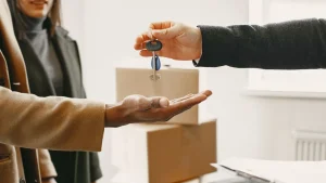 Zwei Personen uebergeben sich die Schluessel einer neuen Wohnung vor Umzugskartons